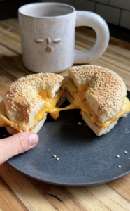 A bagel sandwich with cottage cheese folded eggs sits on a plate with a cup of coffee in the background.