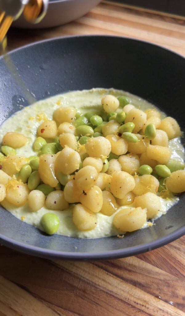 Crispy gnocchi and edamame are plated in a shallow bowl with a green dip.