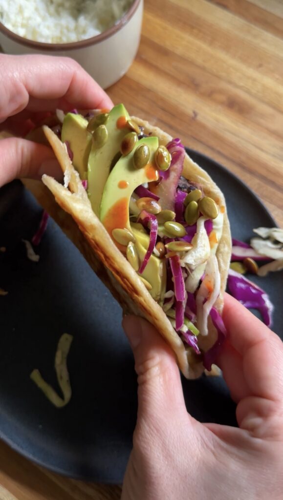 Hands holding black bean tacos above a dark plate.