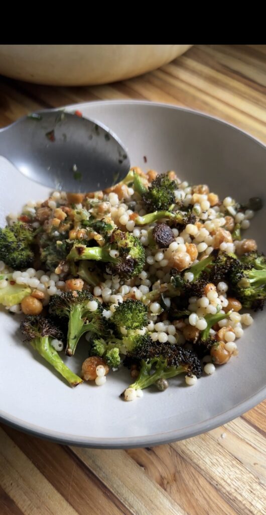 spooning into lemony broccoli chickpea bowls on a wooden cutting board