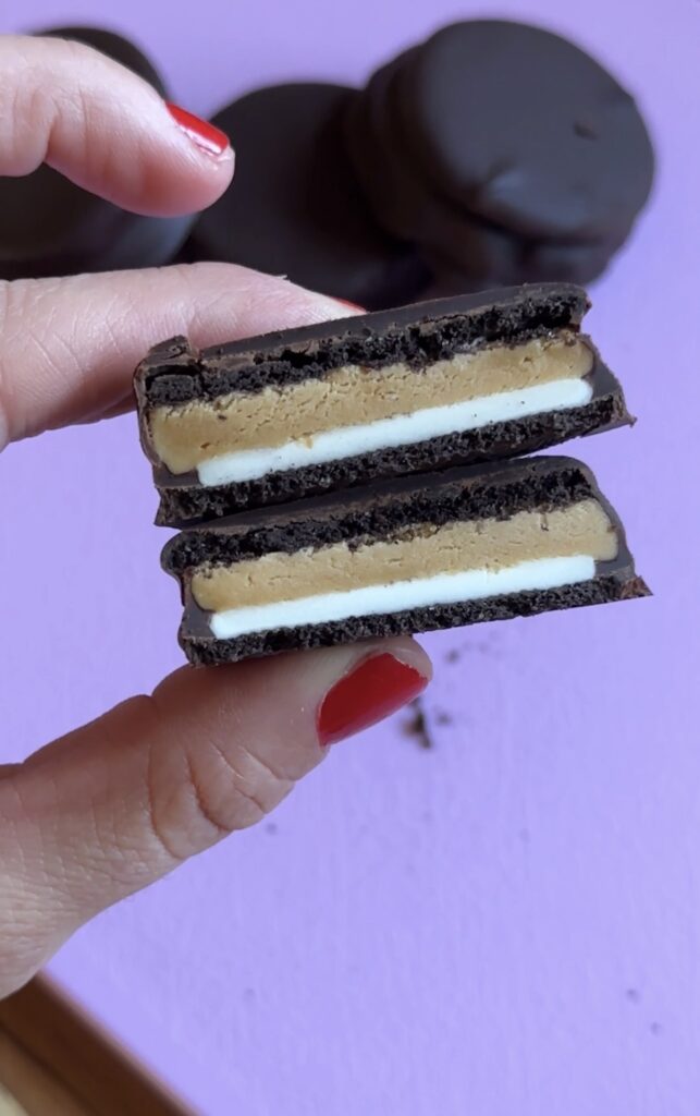 hand holding peanut butter protein oreos above a purple cutting board