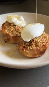 air fryer apple crisp topped with yogurt and being drizzled with honey