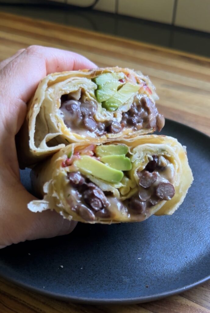 hand holding a cottage cheese breakfast burrito over a dark plate