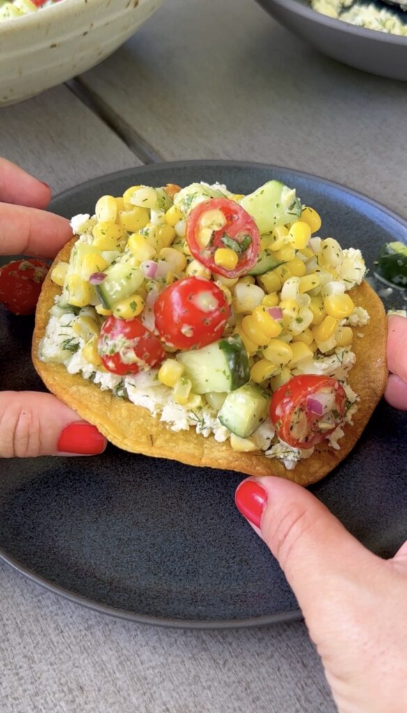 hands holding a smashed feta tostada over a black plate