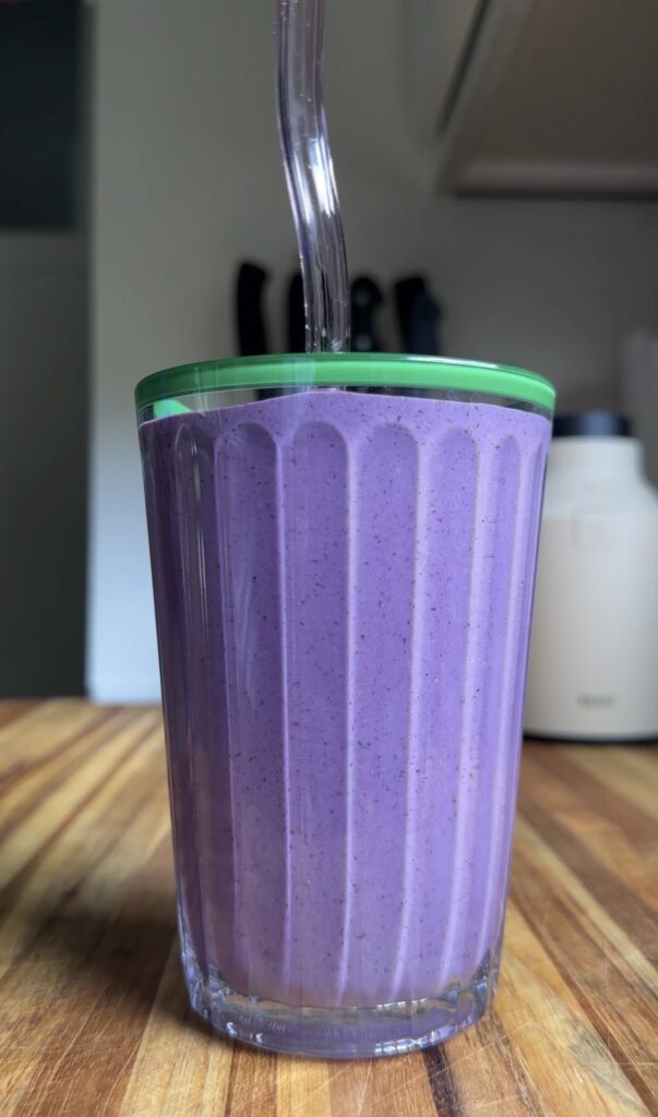 blueberry peanut butter smoothie with a straw sitting on wooden cutting board