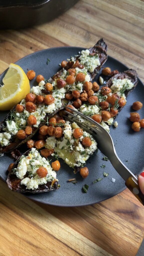 fork slicing into the smashed feta zucchini boats on a dark plate