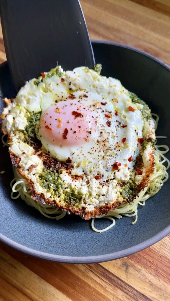 feta fried egg pesto pasta in a dark shallow bowl