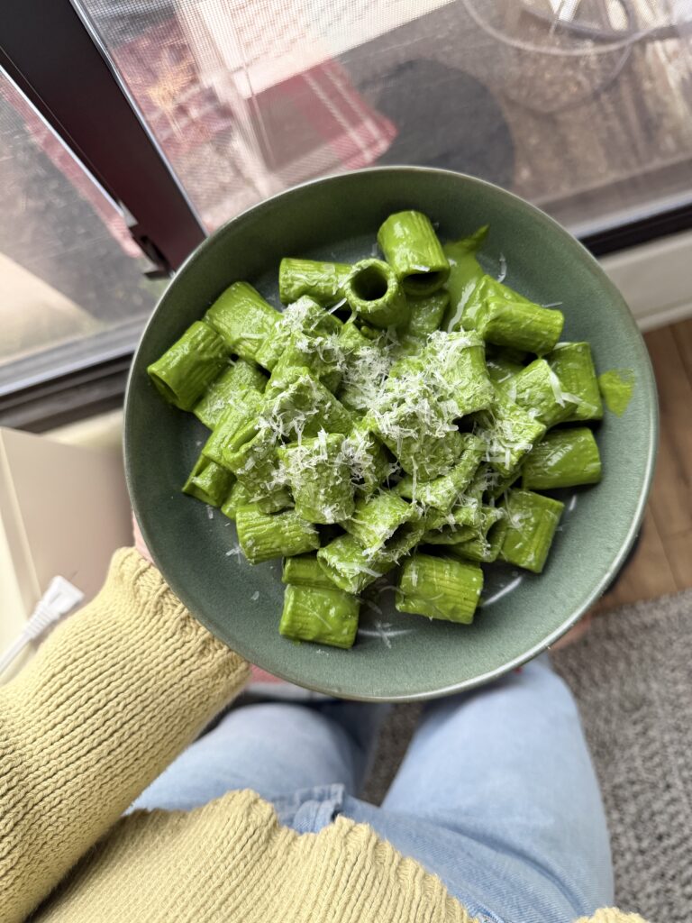 hand holding a bowl of kale sauce pasta