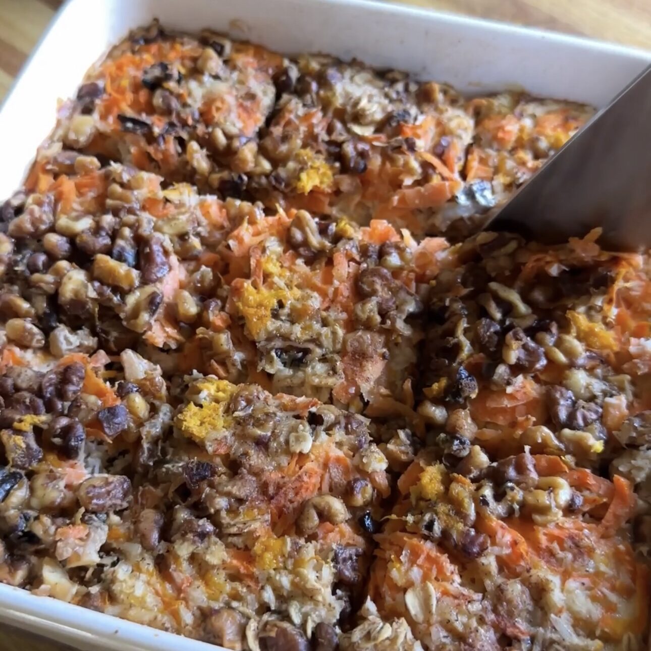 7 layer magic oatmeal bars being cut with a wooden spatula in a baking dish.