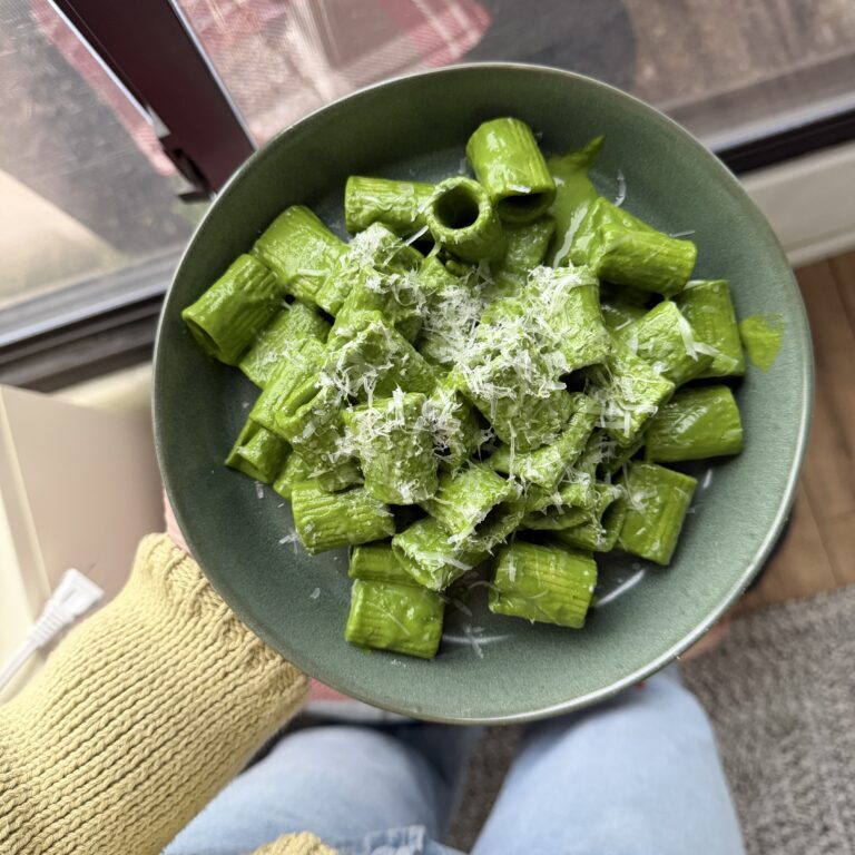 hand holding a bowl of kale sauce pasta