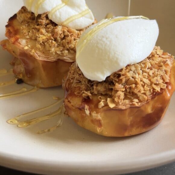 air fryer apple crisp topped with yogurt and being drizzled with honey