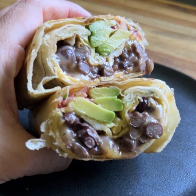 hand holding a cottage cheese breakfast burrito over a dark plate