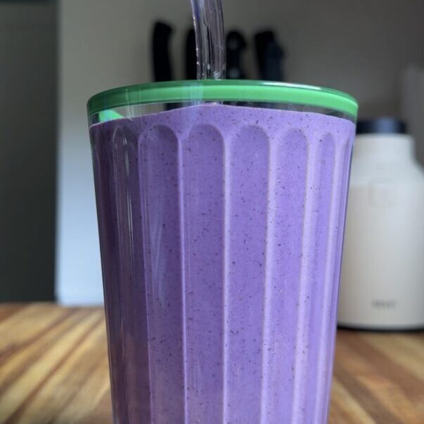 blueberry peanut butter smoothie with a straw sitting on wooden cutting board