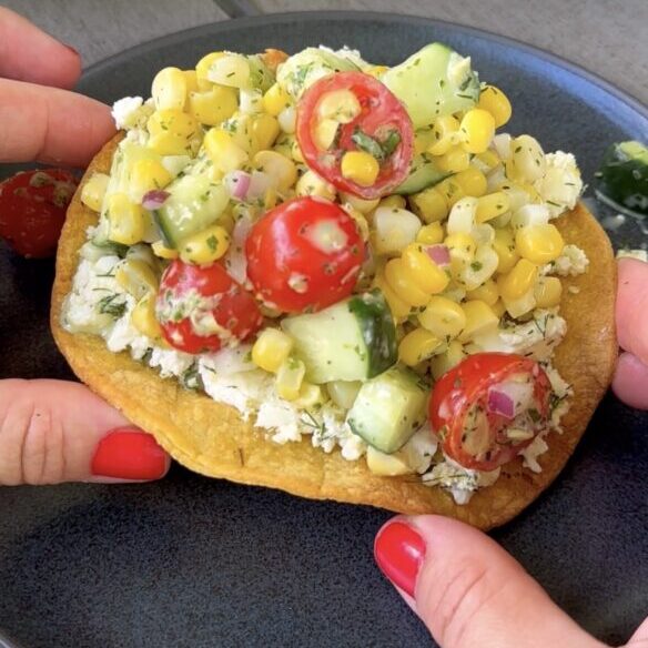 hands holding a smashed feta tostada over a black plate