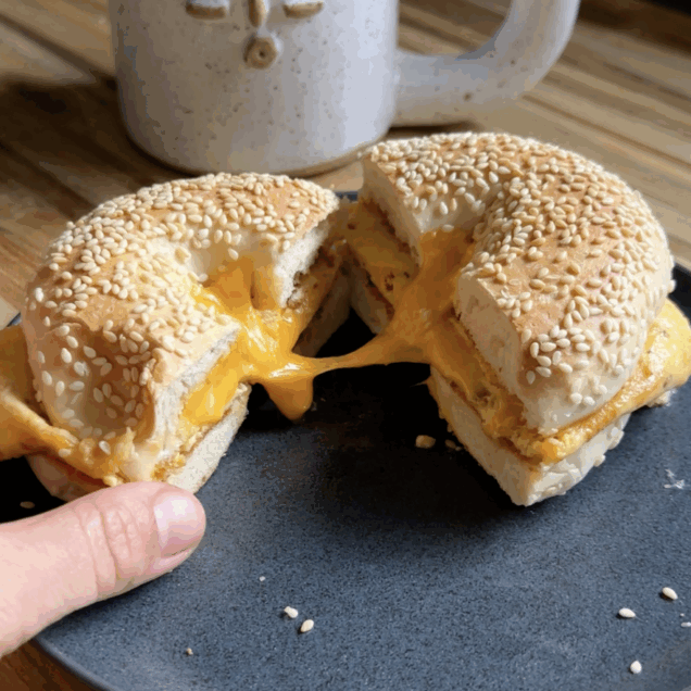A bagel sandwich with cottage cheese folded eggs sits on a plate with a cup of coffee in the background.