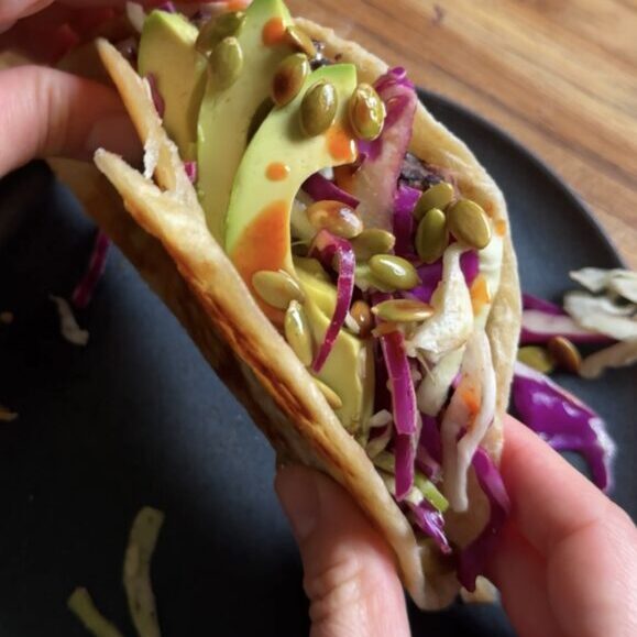 Hands holding black bean tacos above a dark plate.