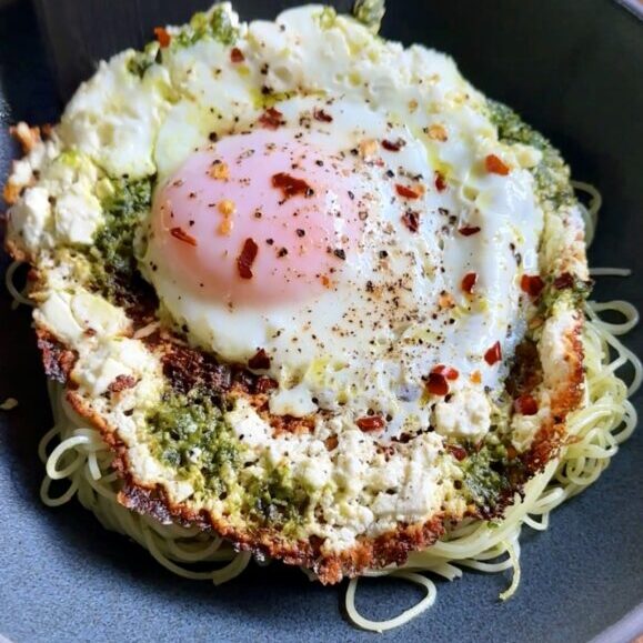 feta fried egg pesto pasta in a dark shallow bowl