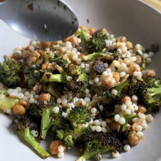 spooning into lemony broccoli chickpea bowls on a wooden cutting board