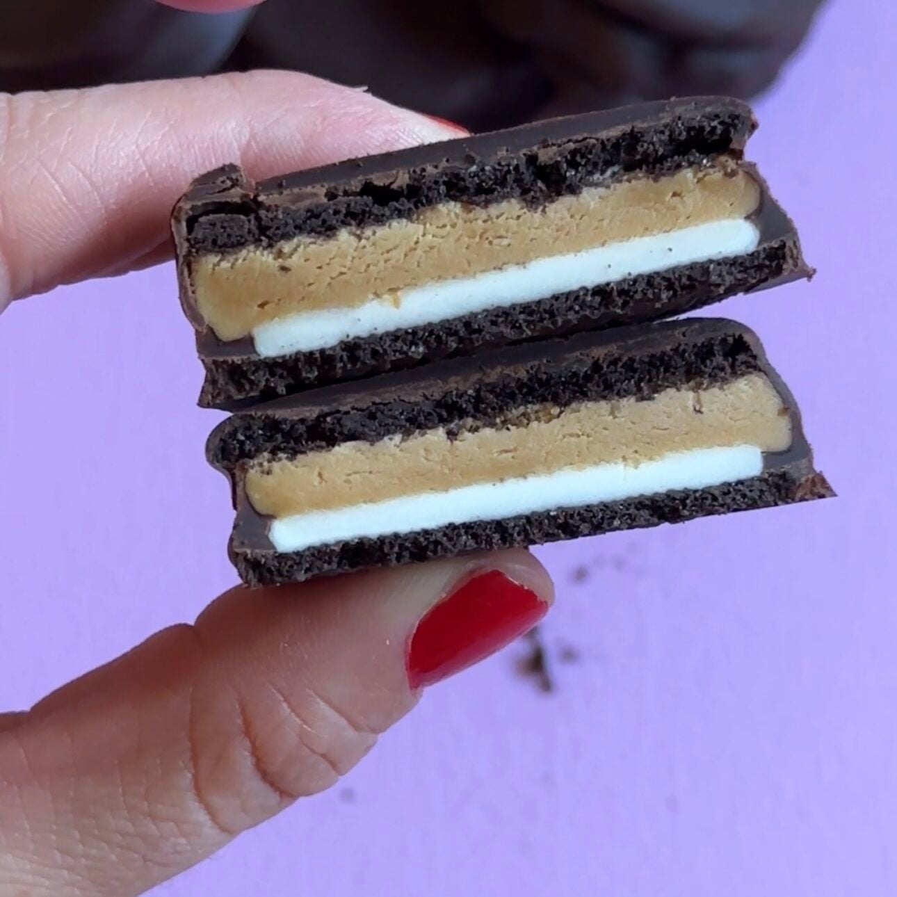 hand holding peanut butter protein oreos above a purple cutting board