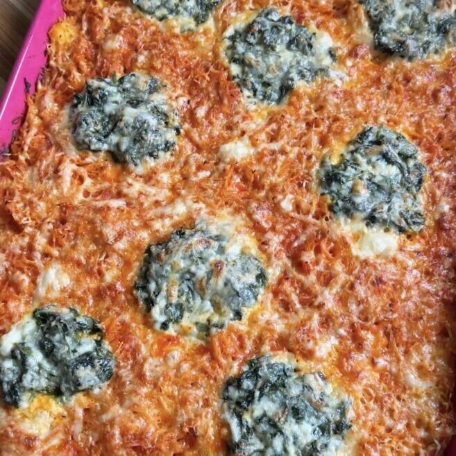 A pink sheet pan with spaghetti squash lasagna topped with a cottage cheese-spinach mixture.