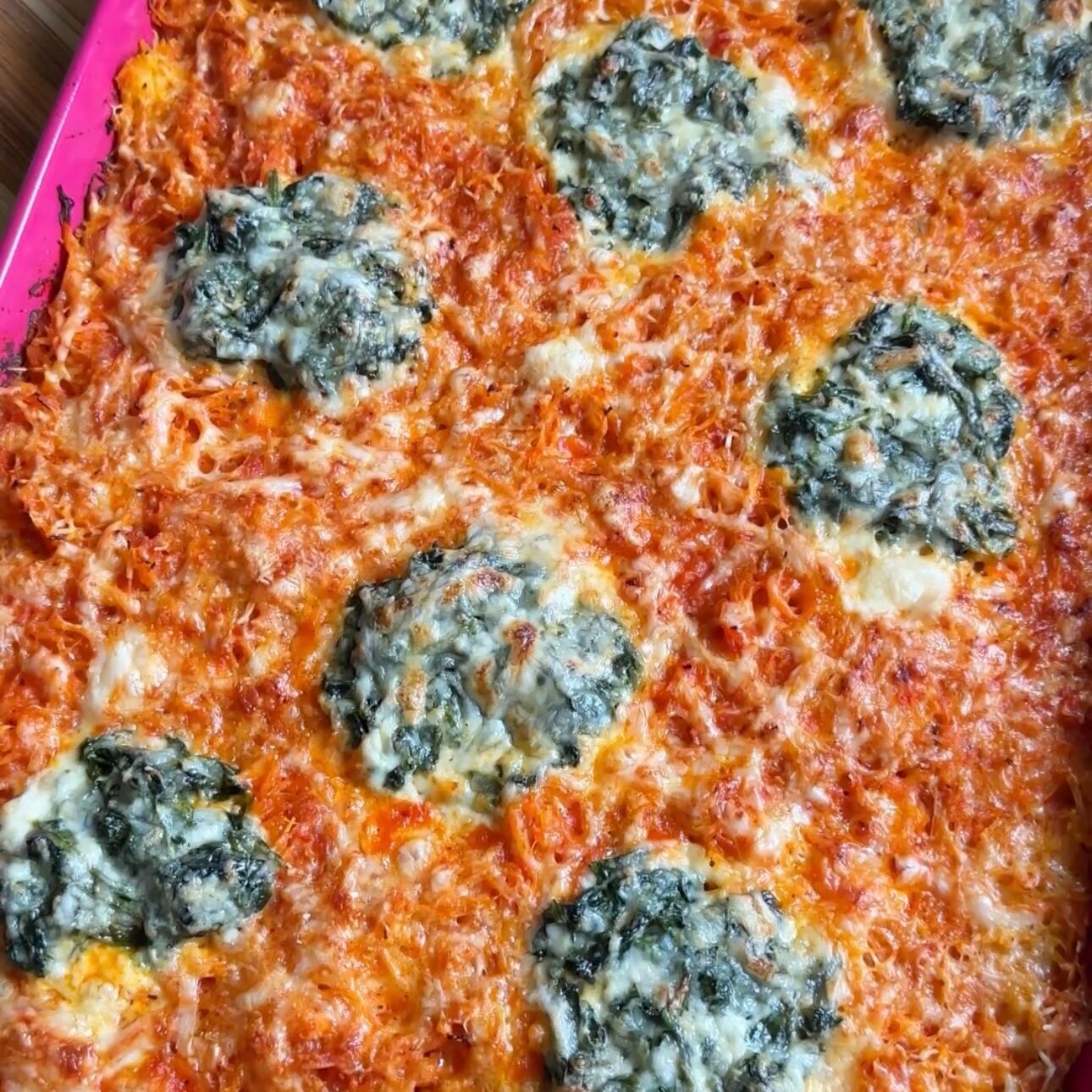 A pink sheet pan with spaghetti squash lasagna topped with a cottage cheese-spinach mixture.