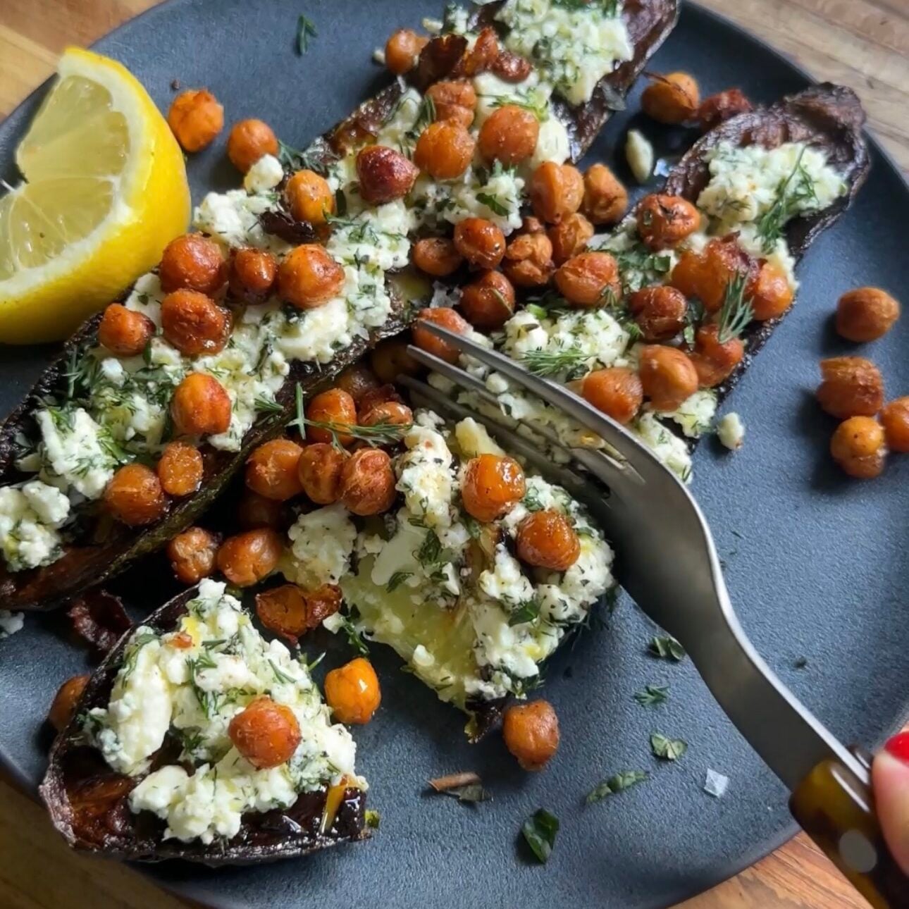 fork slicing into the smashed feta zucchini boats on a dark plate